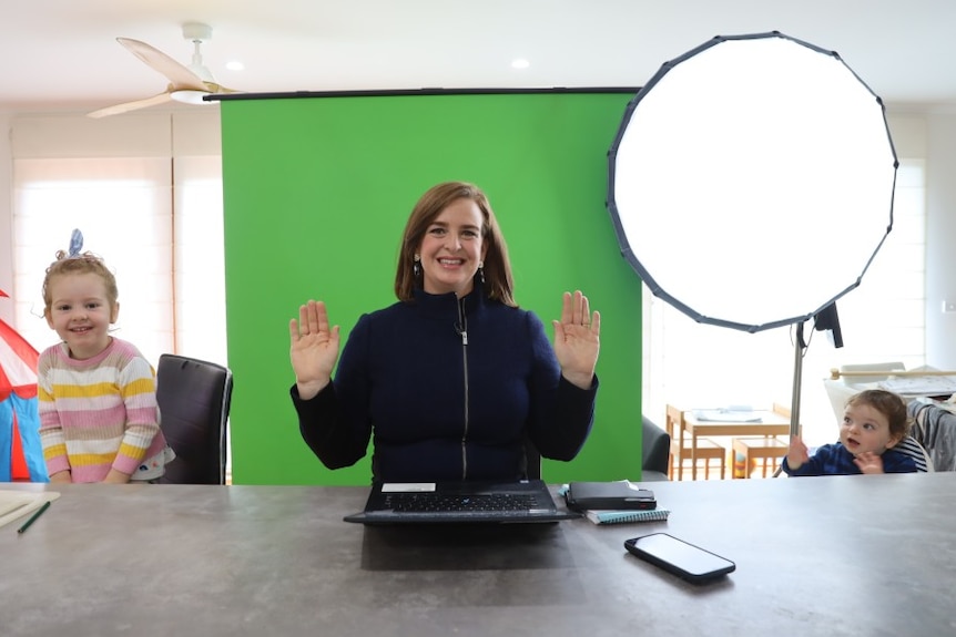 Henderson standing in front of green screen with two children sitting next to her.