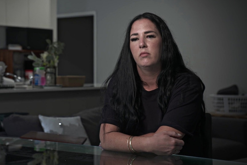 Woman with long dark hair wearing a black shirt sitting at a dining table.
