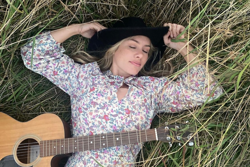Reigan Derry lying on the grass with a guitar on top of her