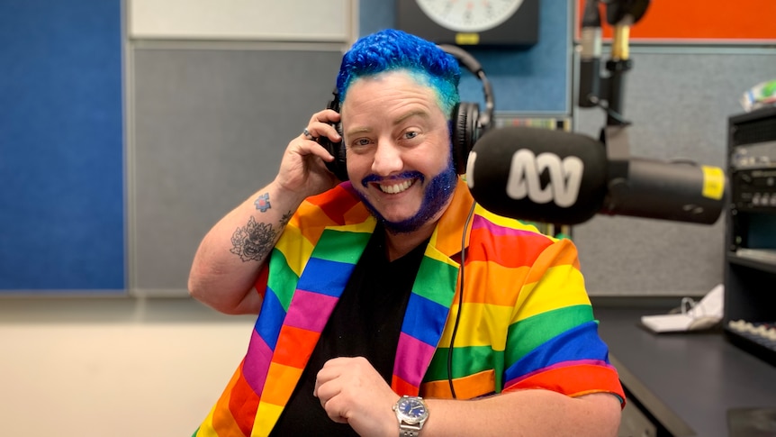 A drag king wears headphones in a radio studio smirking.