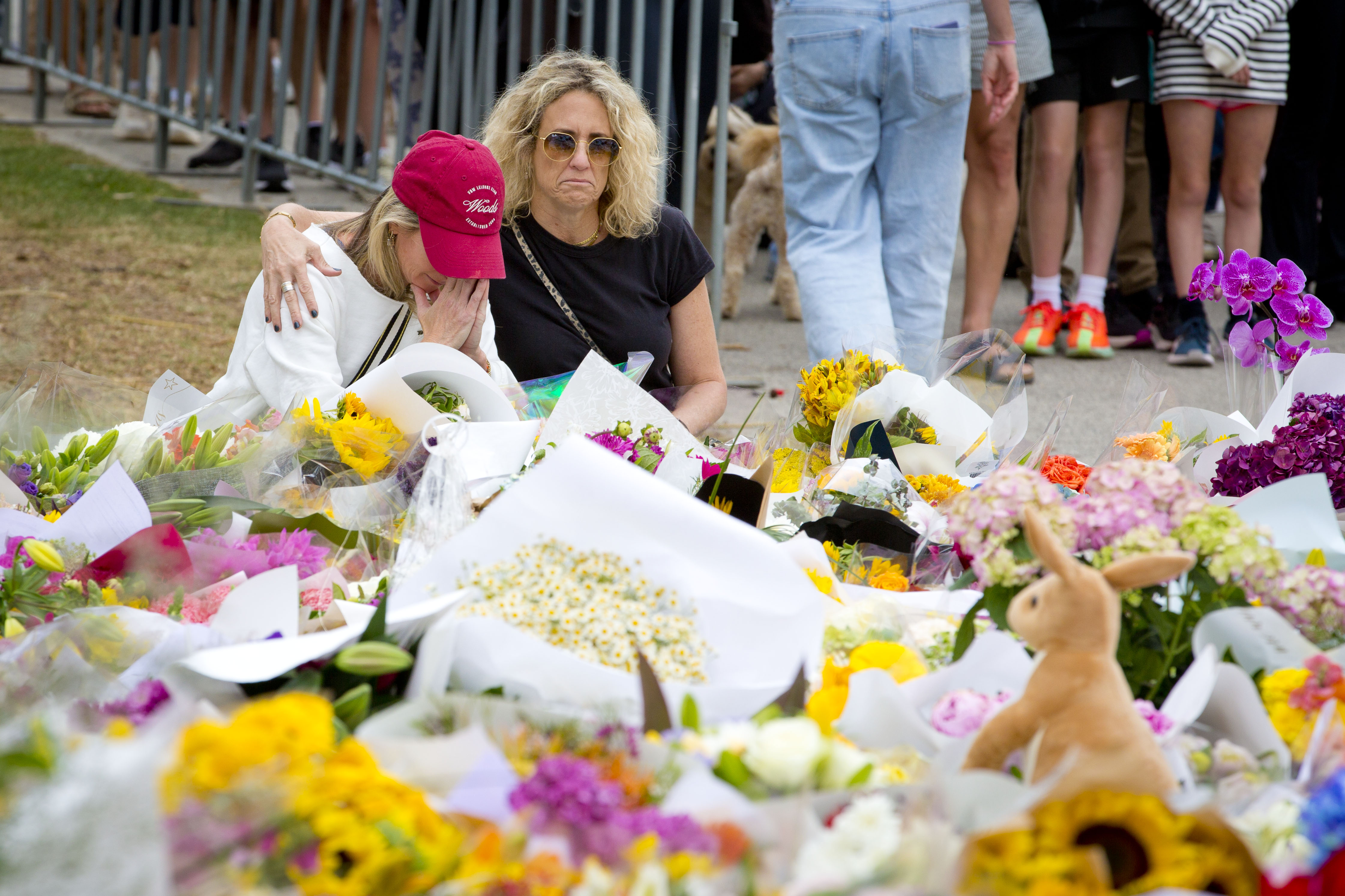 Duas mulheres sentam e choram diante de uma crescente homenagem floral 