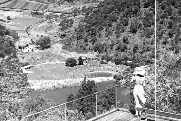 Black and white photo of a lady wearing hat looking down onto a pool and a river