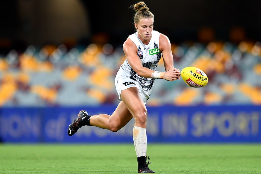 An AFLW player attempts to grab the ball as she runs downfield during a match. 