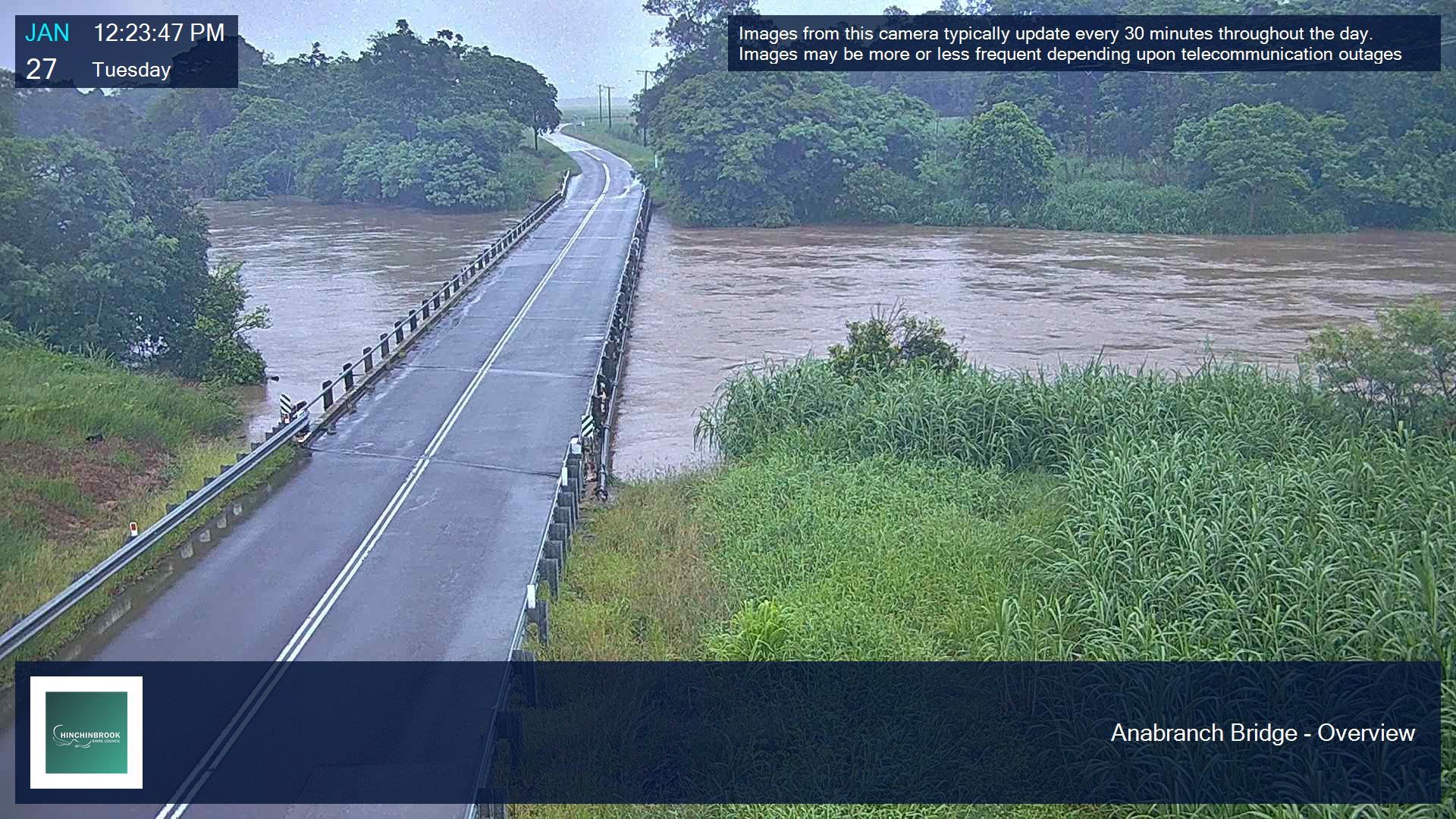 Un río crecido casi alcanza la altura de una presa en una zona rural.