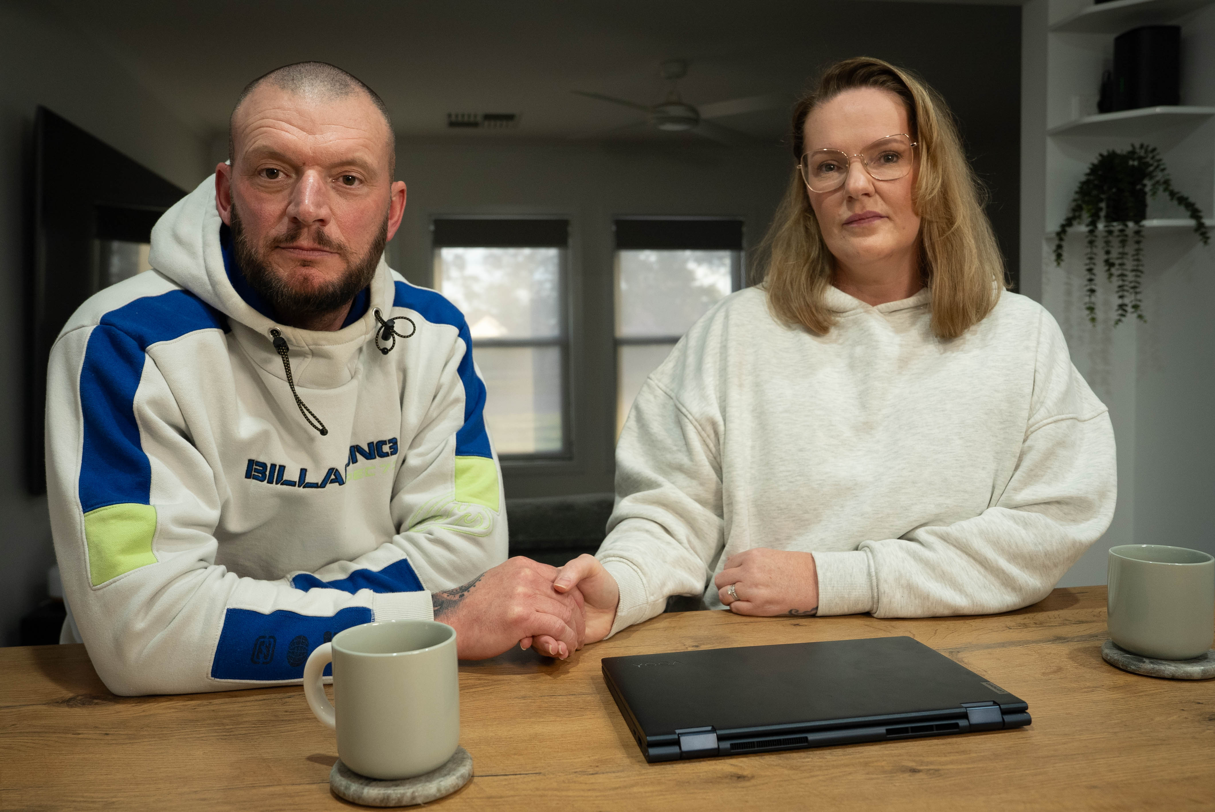 A bearded man and his midwife wife hold hands at their kitchen table in Whyalla