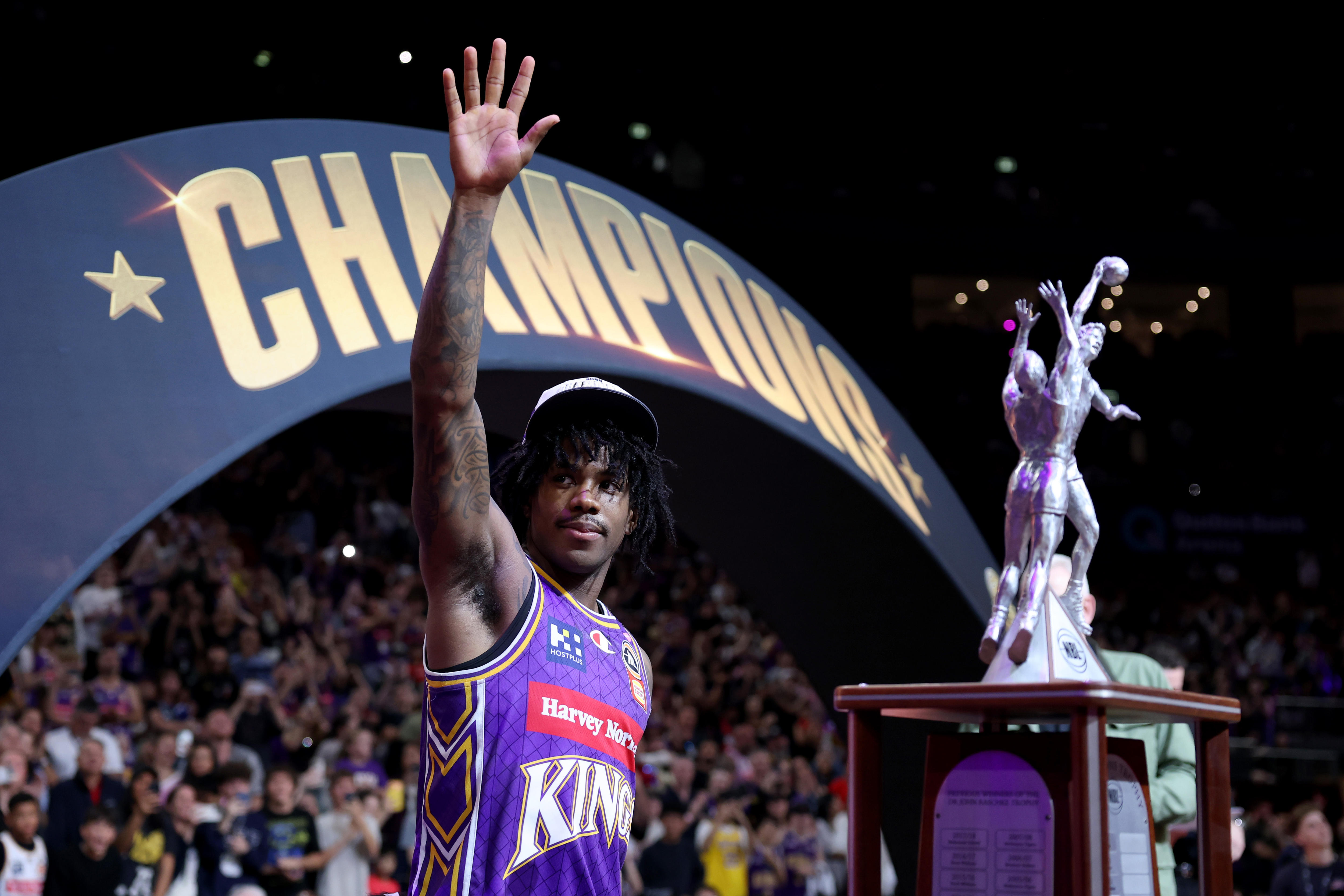 Sydney Kings player Kendric Davis waves to the crowd alongside the NBL championship trophy.