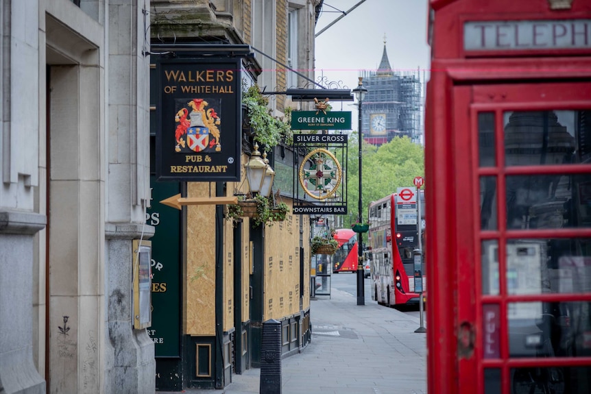 A boarded up pub with a red telephone box in the foreground and Big Ben in the background