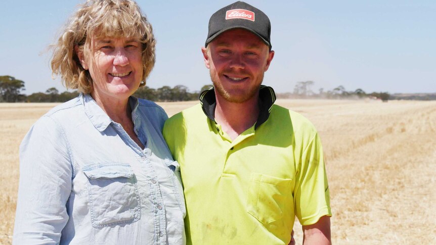 Young man in cap stands in wheat field with an older woman in blue shirt