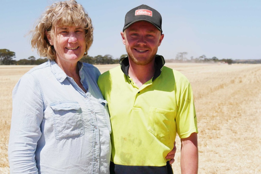 Young man in cap stands in wheat field with an older woman in blue shirt