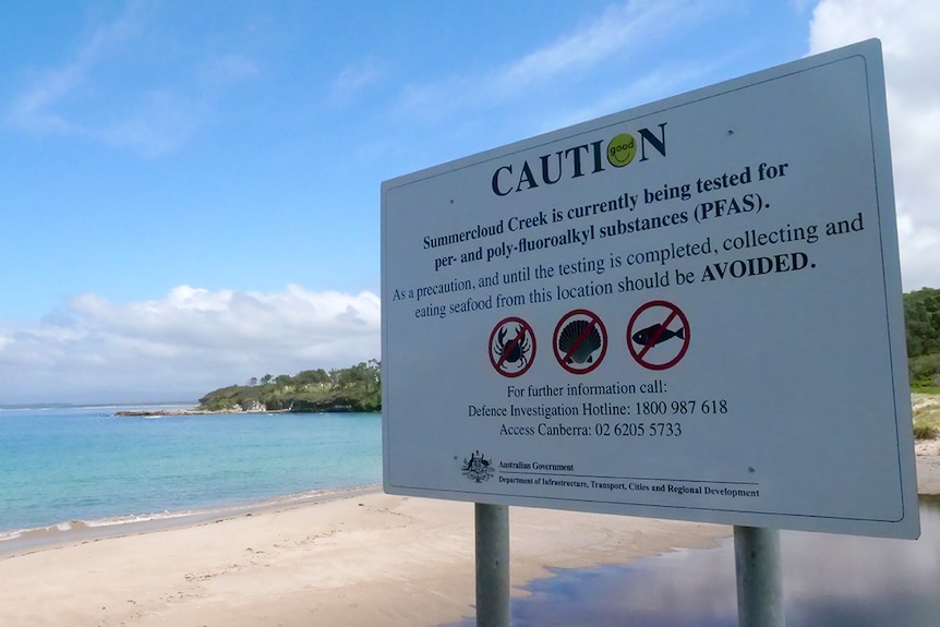 A sign warning of PFAS contamination in Summercloud Creek with the beach in the background.