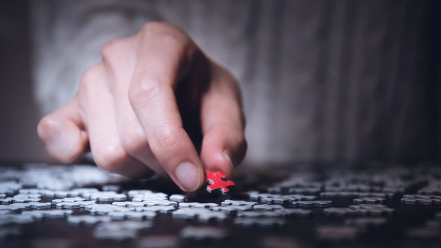 Hand reaches out to pick up a piece of a puzzle on a table.