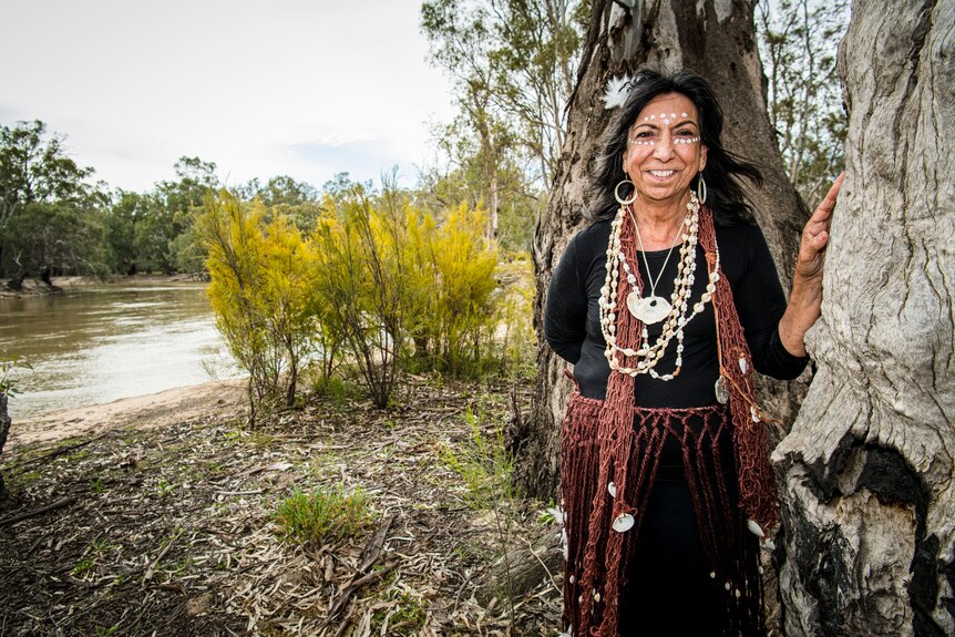 A woman stands next to a tree with a large river in the background.