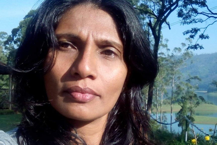 A selfie of Darshika Withana outside in a regional area with green hills, trees and a lake in the background.