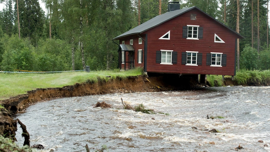 A house hangs over a rain-swollen creek as floods sweep through parts of Sweden.