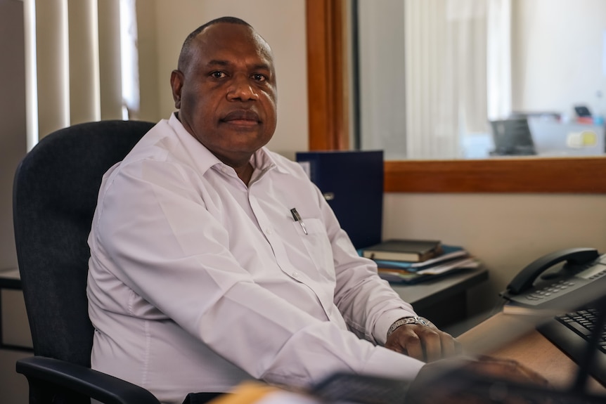 A man in a business shirt sits at a desk 