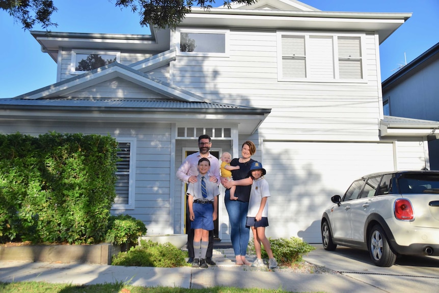 Steve and Bev Jones pose for a photo with their children in front of a grey two storey house
