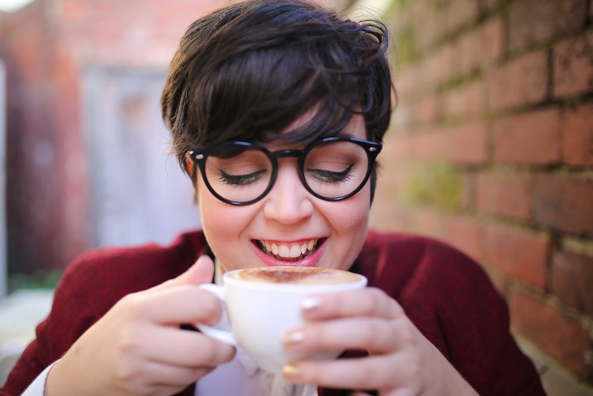 A smiling woman drinks a cup of coffee (generic) on May 3, 2017.