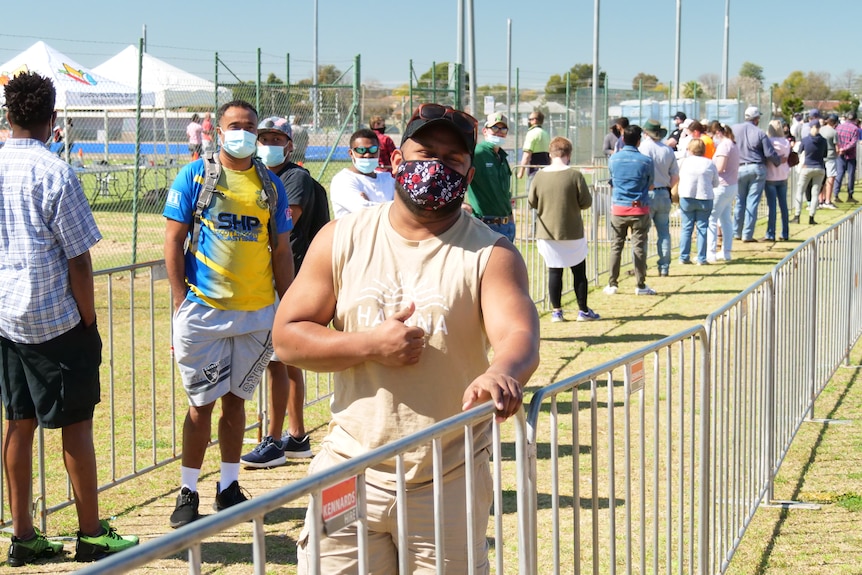 A man standing in line with his thumb up.