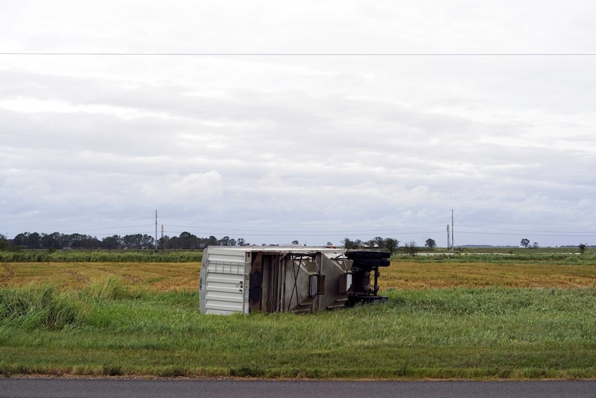 A semi-trailer flipped on its side, lays in a field.