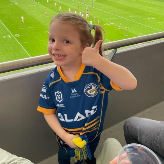 A young girl gives the thumbs up while wearing a Parramatta Eels jersey.