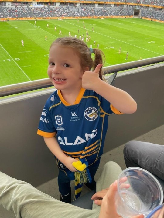 A young girl gives the thumbs up while wearing a Parramatta Eels jersey.