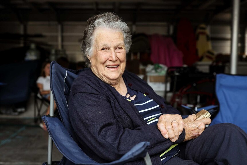 A woman with grey hair sits smiling on a camping chair