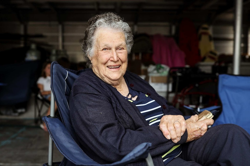 A woman with grey hair sits smiling on a camping chair