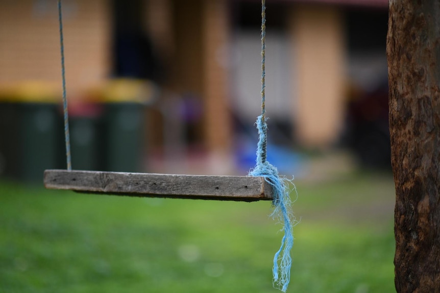 A swing with a blue rope tied to it with a blurred house in the background
