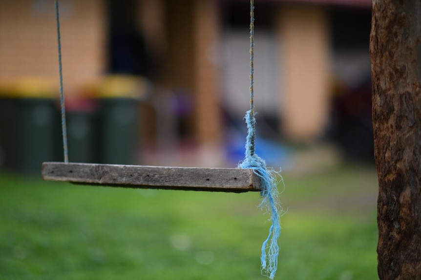 Une balançoire avec une corde bleue attachée avec une maison floue en arrière-plan