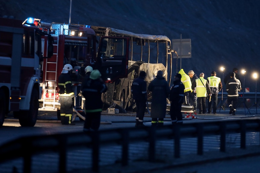 Emergency service workers surround a burnt bus on a road