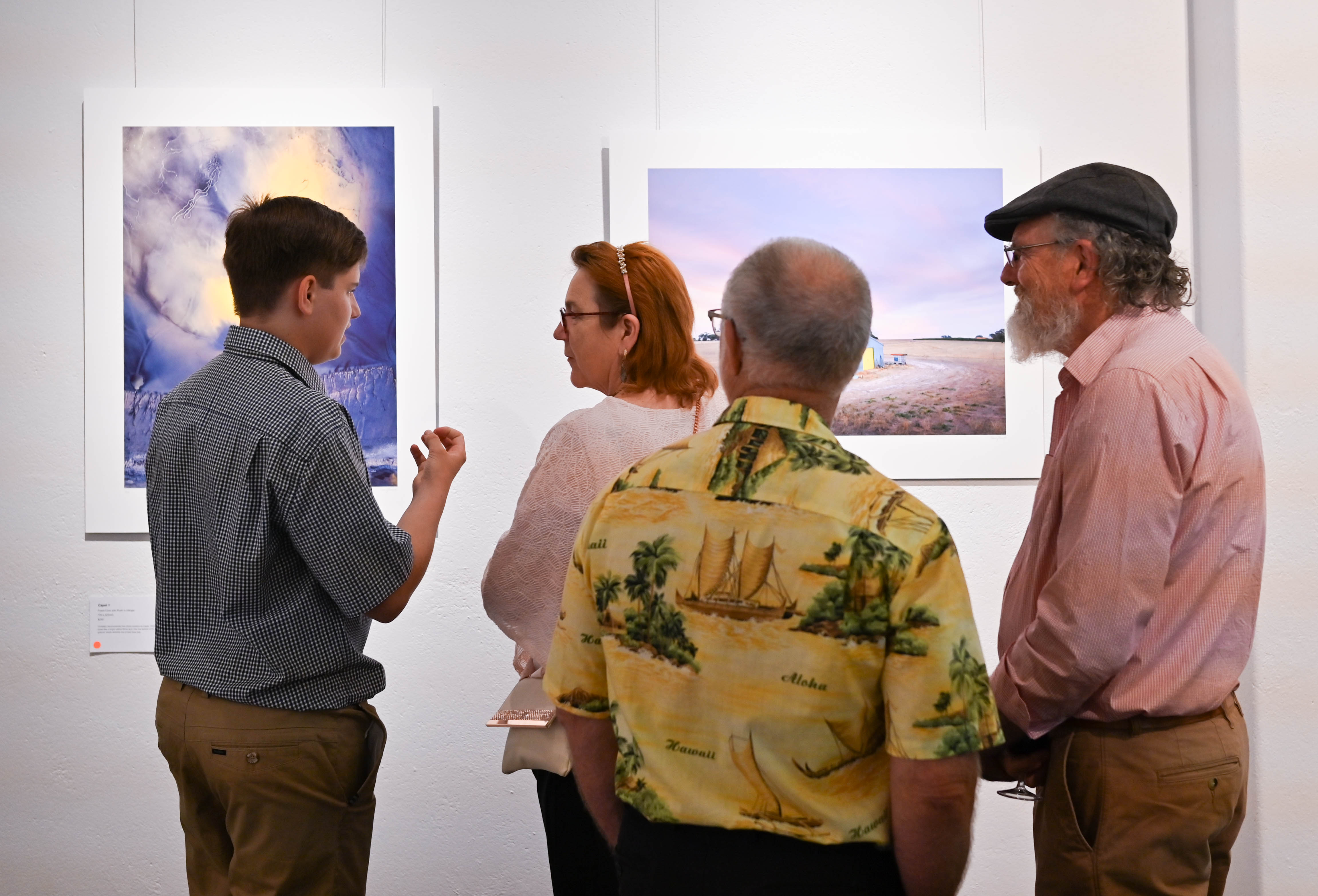 A young man speaks to a woman at an art gallery as two older men listen.