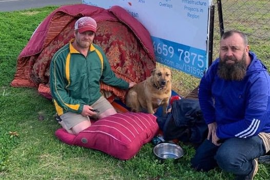 A man sits in the grass with his dog. 