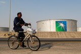 A man rides a bicycle past oil tanks 
