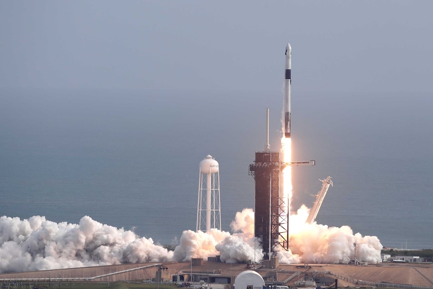 A rocket lifts off from a launch pad during the day, there is fire and smoke clouds coming out of the bottom