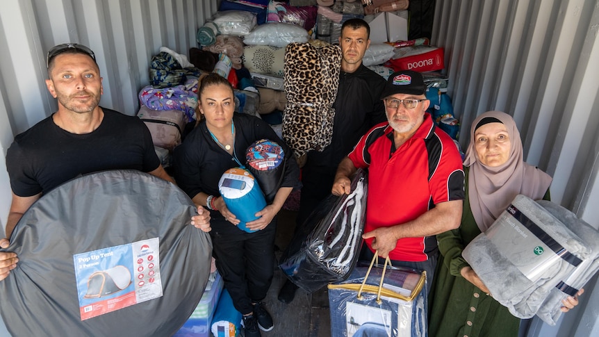 A group of people hold sleeping bags and blankets in a shipping container.