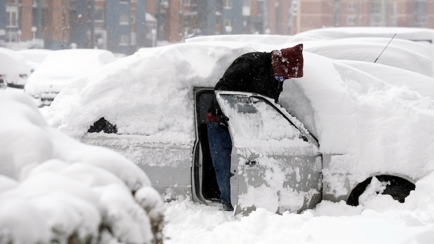 A man opens the door of his snow-covered car in Kosovo's capital Pristina on January 26, 2012.