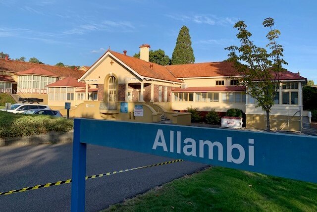 A blue sign reading Allambi in front of an older-style redbrick and rendered building.