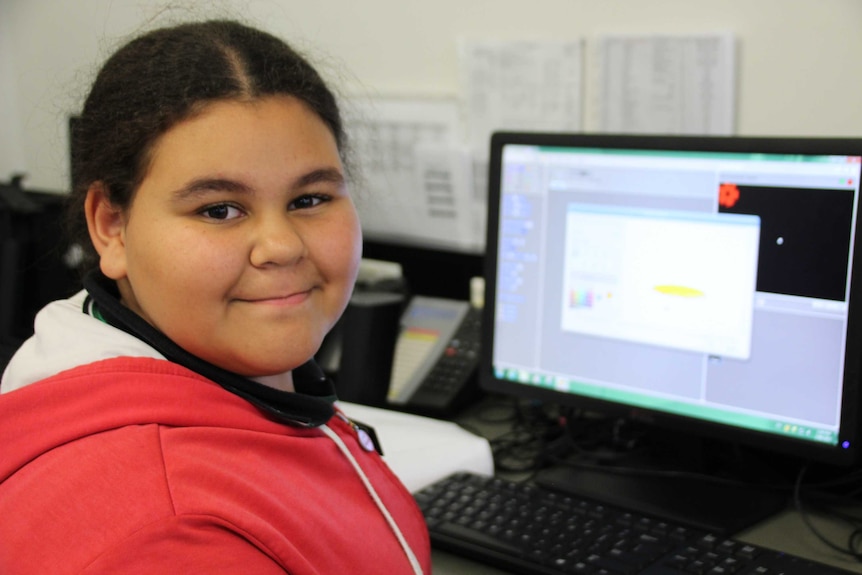 Primary school student, Lily, sits in front of a computer, smiling at the camera.