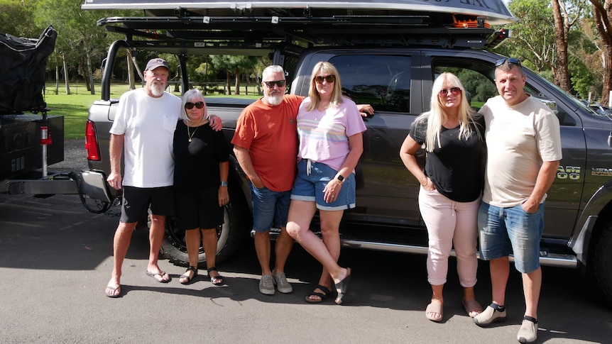 6 people stand in front of a 4wd at a caravan park 
