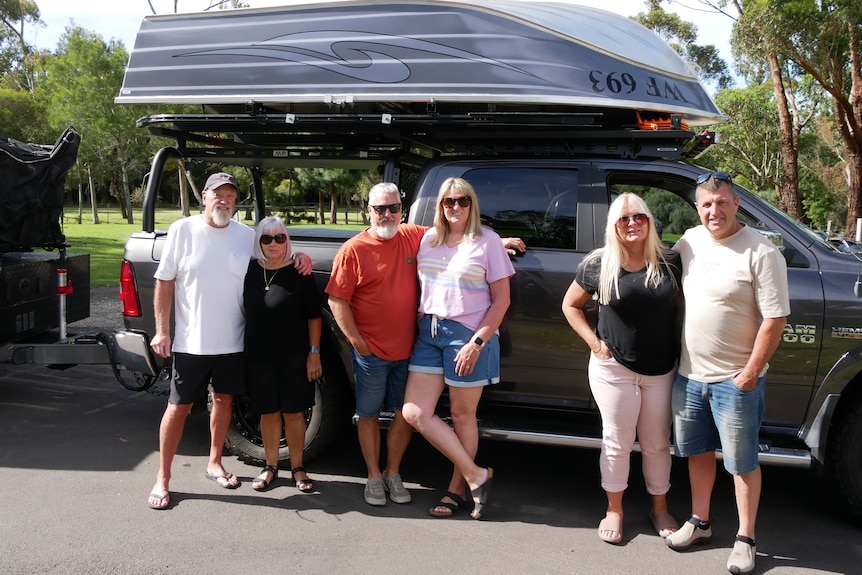 6 people stand in front of a 4wd at a caravan park 