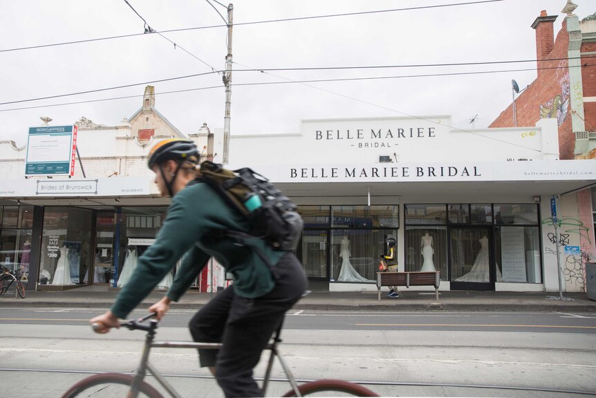 A cyclist rides past a store named Belle Mariee Bridal