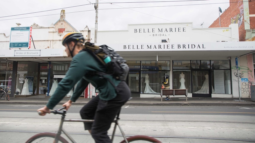 A cyclist rides past a store named Belle Mariee Bridal
