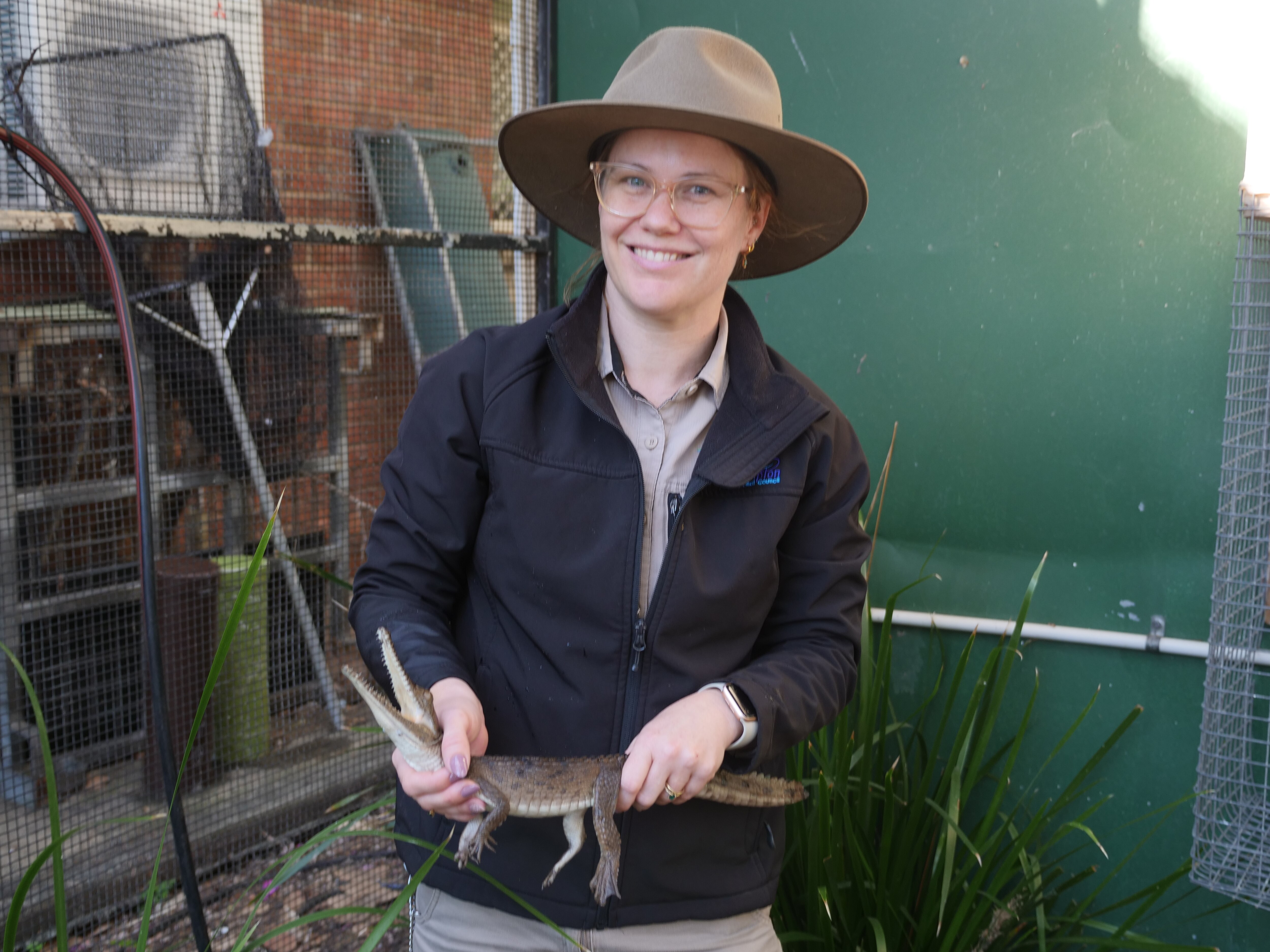 Young woman wearing an Akubra style hat holding baby crocodile, smiling at camera