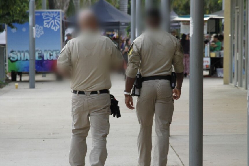 Two men in khaki clothing walk down a street. They are seen from behind. 