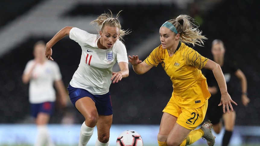 Two women, one in yellow, one in white, chase after a ball