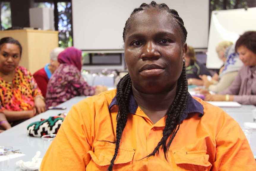 Portrait of a woman with long plaits in an orange work shirt.