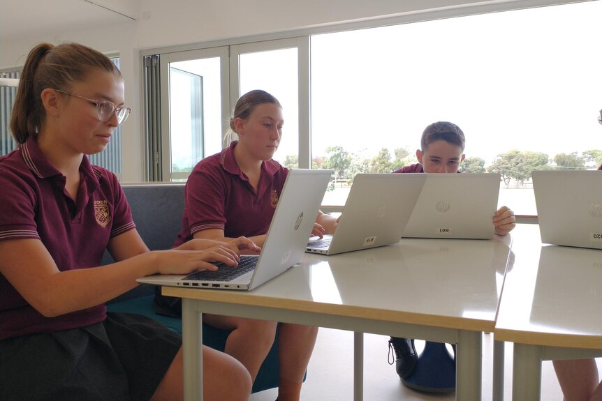 A group of students sitting around a table with their laptops out. 