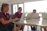 A group of students sitting around a table with their laptops out. 