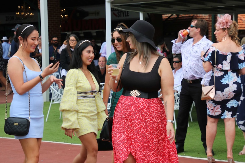 Crowds of horse racing fans drink and stand around