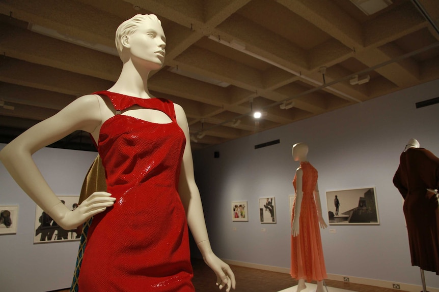 A mannequin wears a red vintage dress with pictures of famous fashion photography behind.